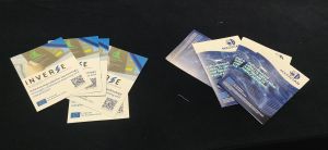 Two different staples of flyers on a black table: INVERSE flyer with QR code and MAGICIAN flyer
